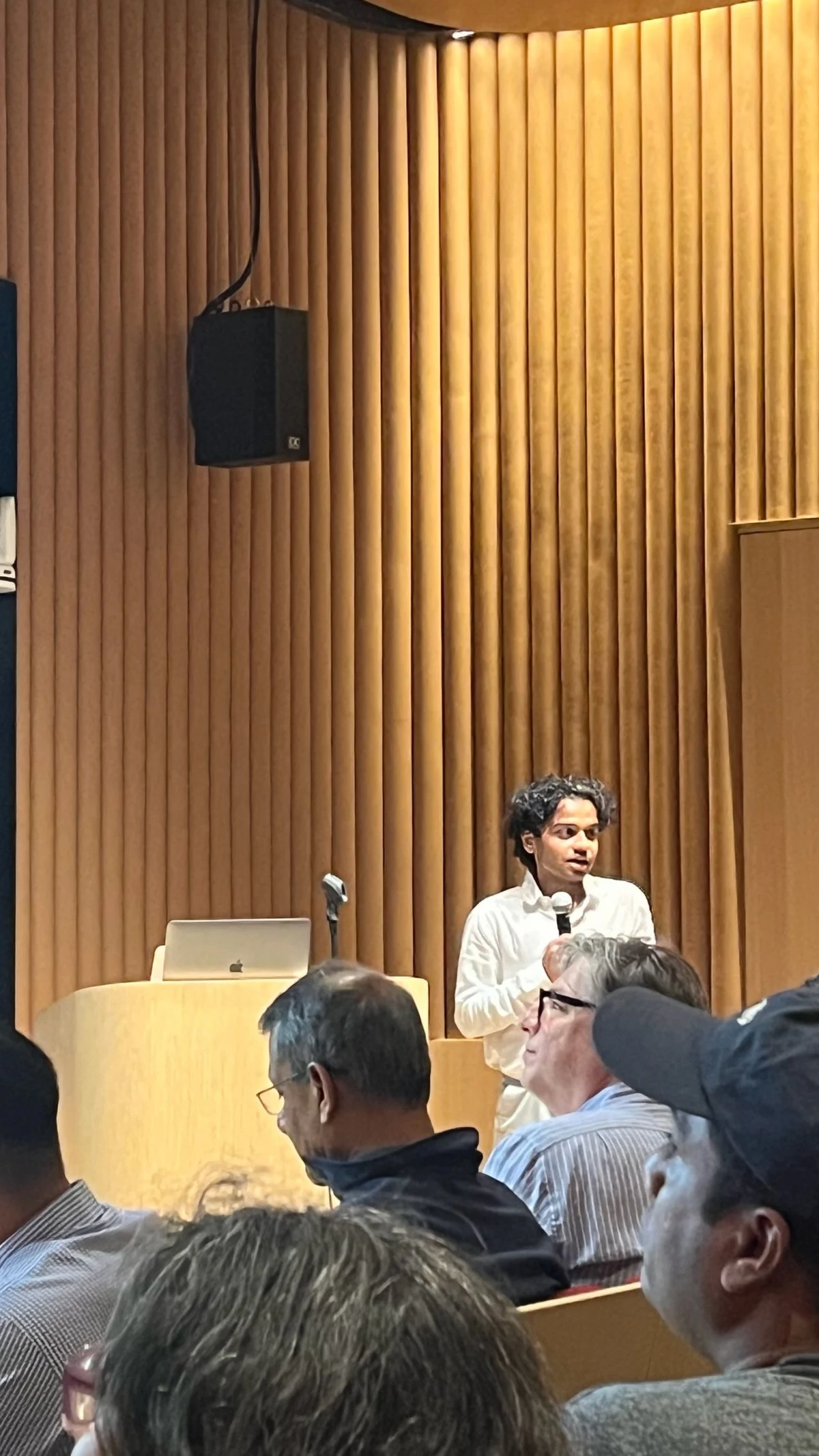 Dhruv speaking into a microphone at a podium in front of an audience